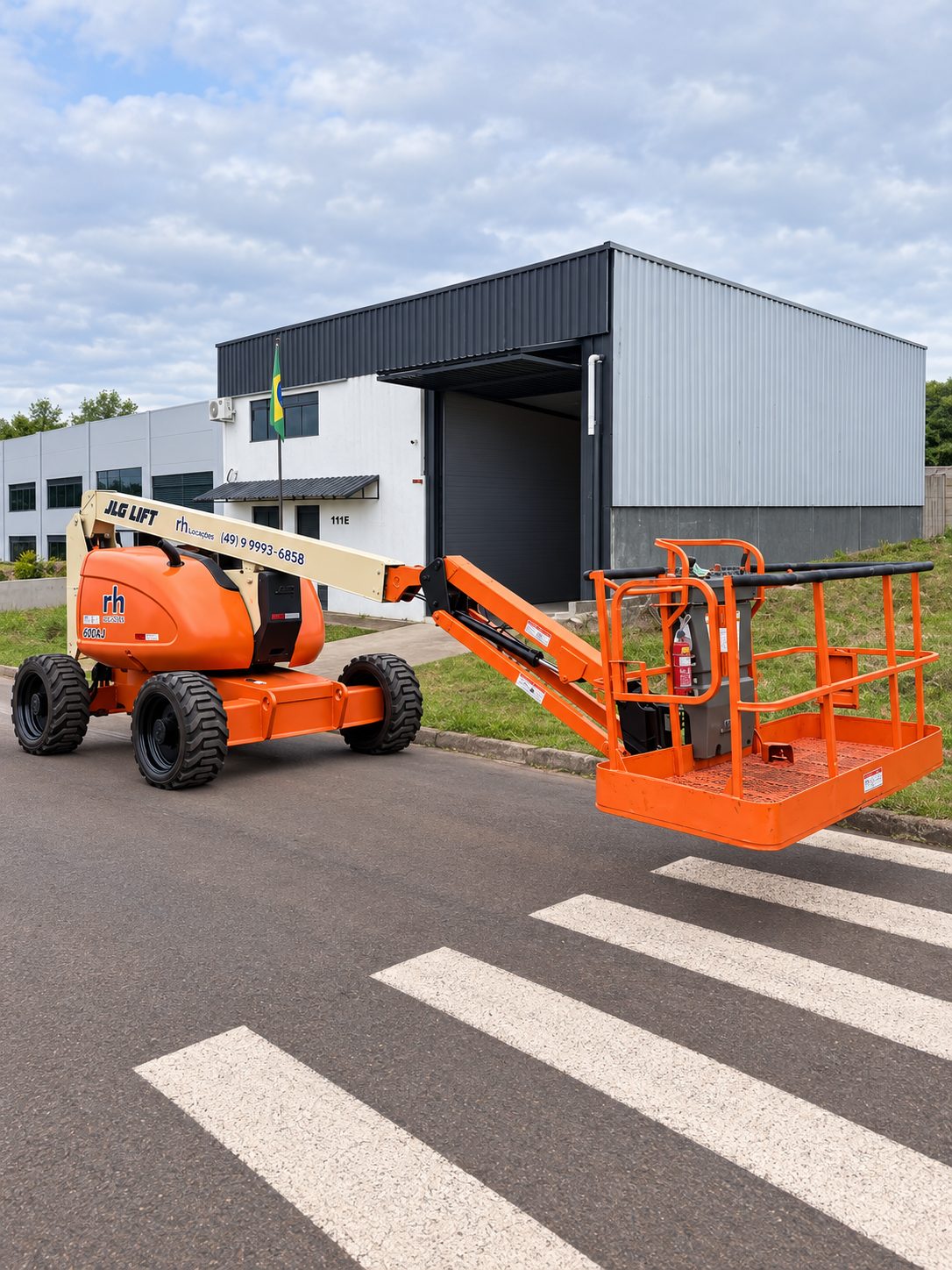 JLG 600AJ da rh Locações com a cesta estendida em frente a um galpão